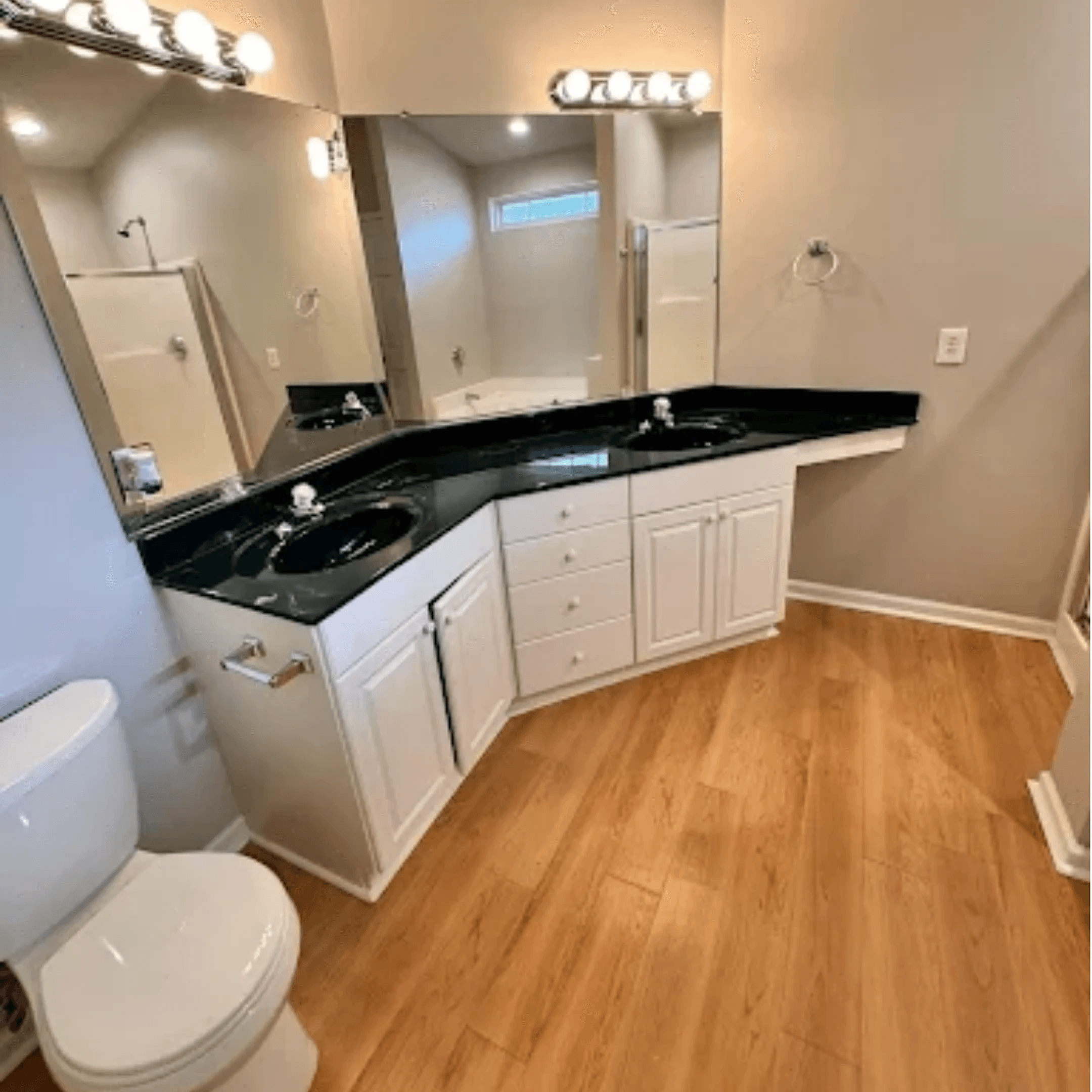 Bathroom with a black granite double vanity, wide mirror and clean wood-look floor, cleaned by Harbor Home Cleaners